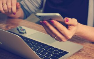 Content Creation Jobs - A woman holding an iPhone in front of a laptop